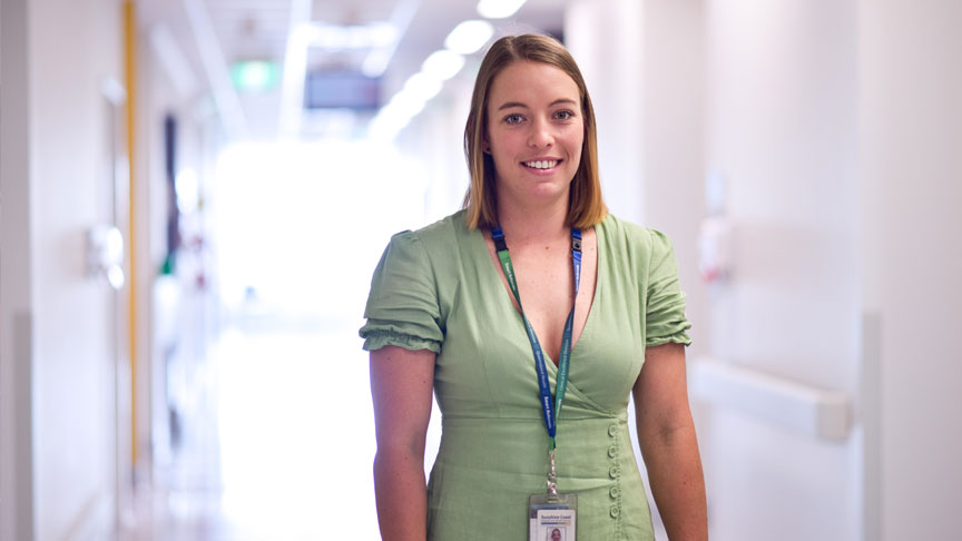 Headshot of Ashleigh Coombs standing in a hospital hallway wearing a green dress