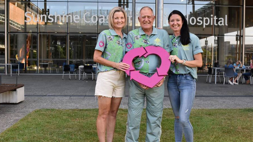 Three people holding the Donate life logo standing on the grass in front of Sunshine Coast University Hospital