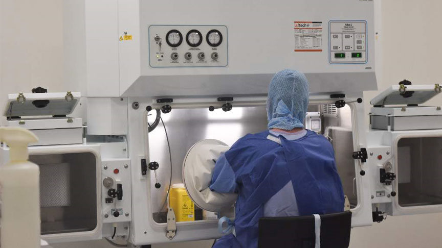 Person wearing PPE sits using the Pharmacy Aseptic Production Unit