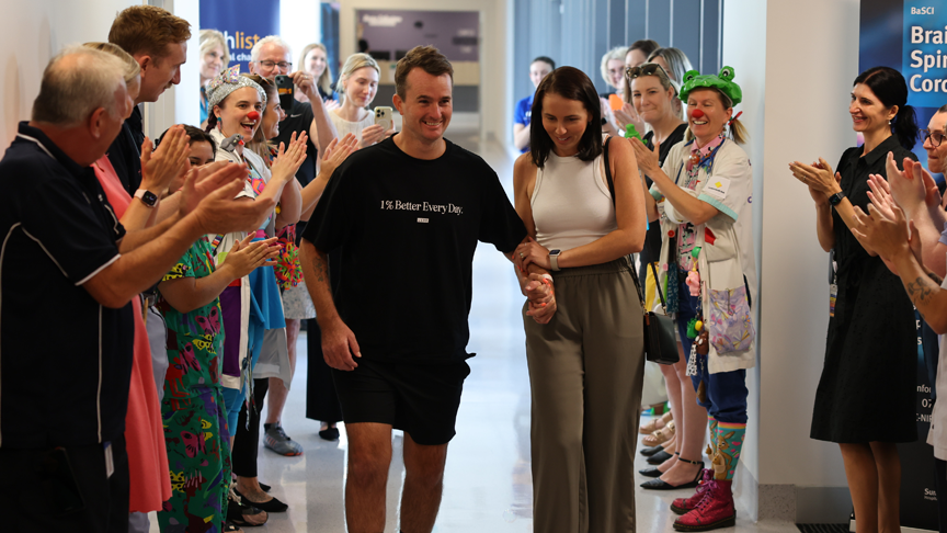 Staff line the hallway clapping as Sunshine Coast University Hospital rehabilitation patient Chris Perry walks out of hospital supported by his wife