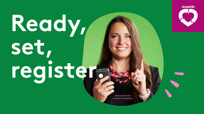 Ready, set, register. Doante Life. A person stands against a green background holding a mobile phone in one hand and raising the index finger on the other hand.