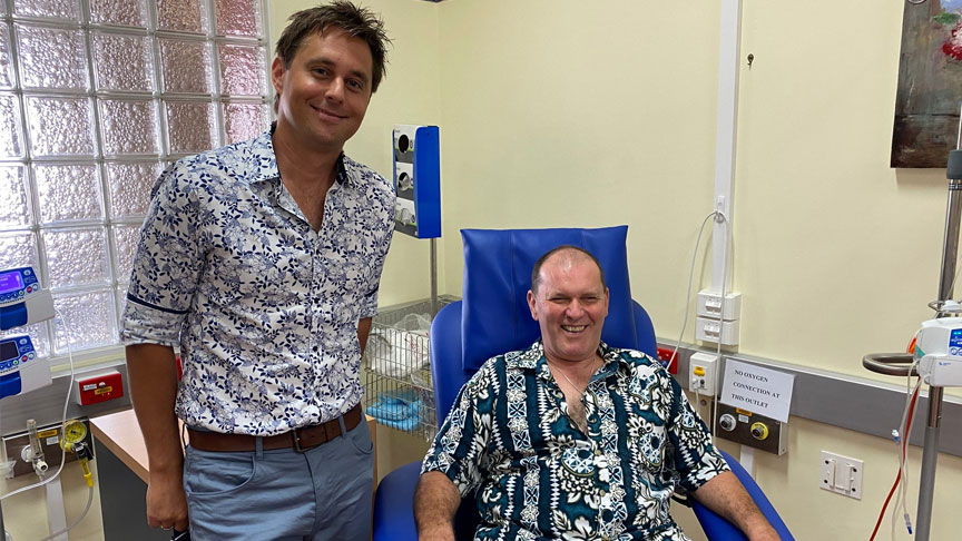 Ben Newman stands next to patient Stuart Gooddy sat in a treatment room at Gympie Hospital