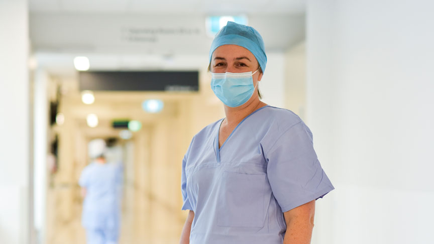 Dr Priscilla Martin standing in a hospital hallway wearing scrubs and a face mask