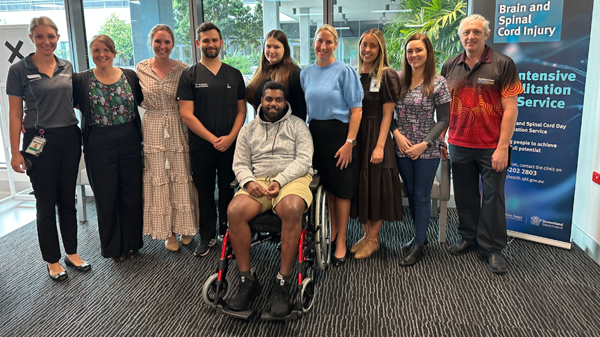 Nine members of the Sunshine Coast Health Rehabilitation team stand behind patient Nemani Ranuve sat in his wheelchair