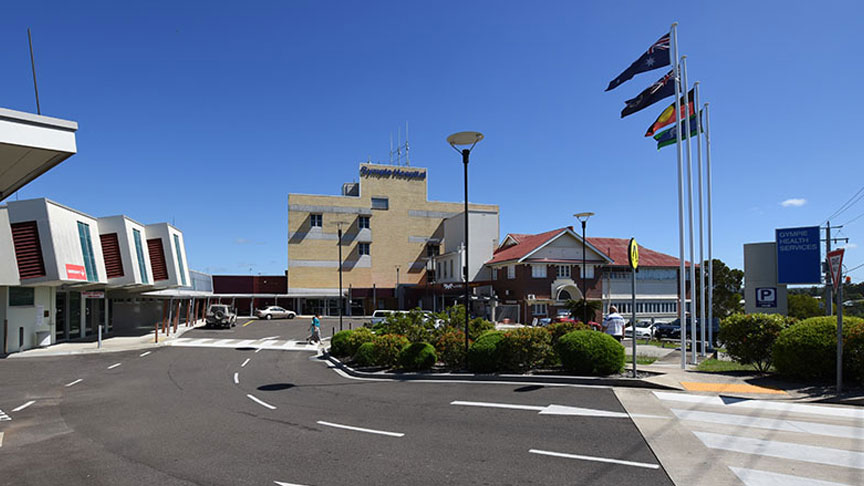 A view of the exterior of Gympie Hospital with the Emergency Department to the left, the main hospital building straight ahead and 4 flag poles to the right