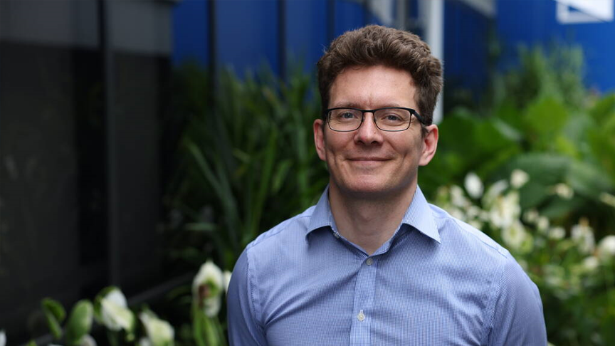 Headshot of Dr Nicolas Smoll standing in front of greenery.