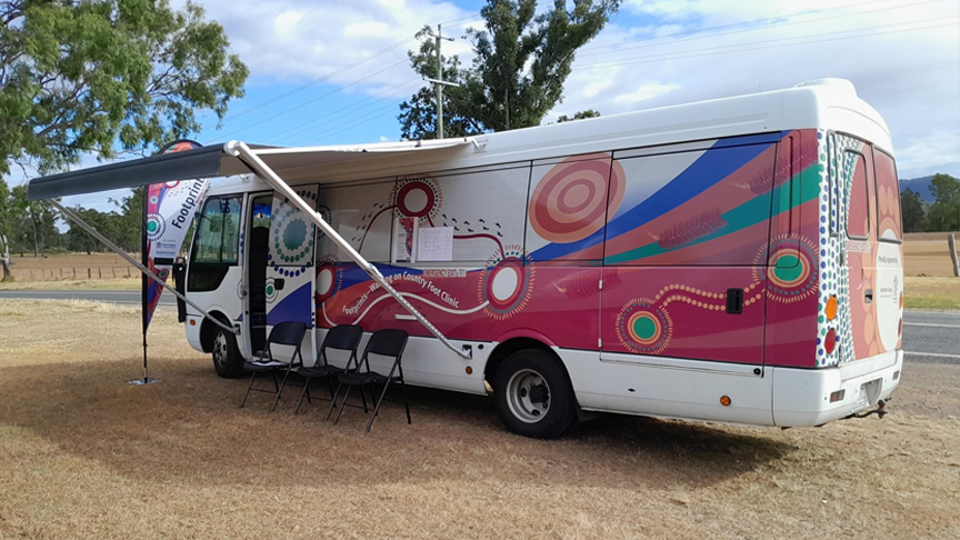 Footprints mobile foot clinic bus parked on the grass next to a road with a side awning up